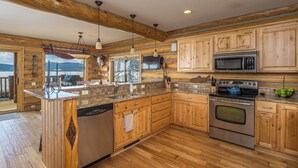 A kitchen with wooden cabinets, a stainless steel stove, a dishwasher, and a large island with a sink. - Hebgen Lakeshore Retreat (West Yellowstone)