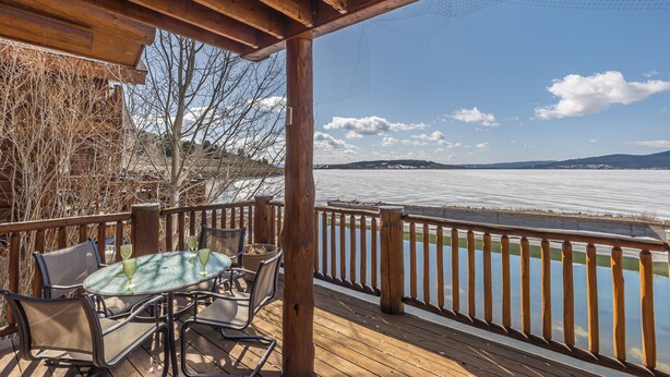 A wooden deck with a table and chairs, overlooking a body of water and distant mountains. - Hebgen Lakeshore Retreat (West Yellowstone)