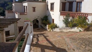 A courtyard with a white building featuring a wooden balcony and a small archway.