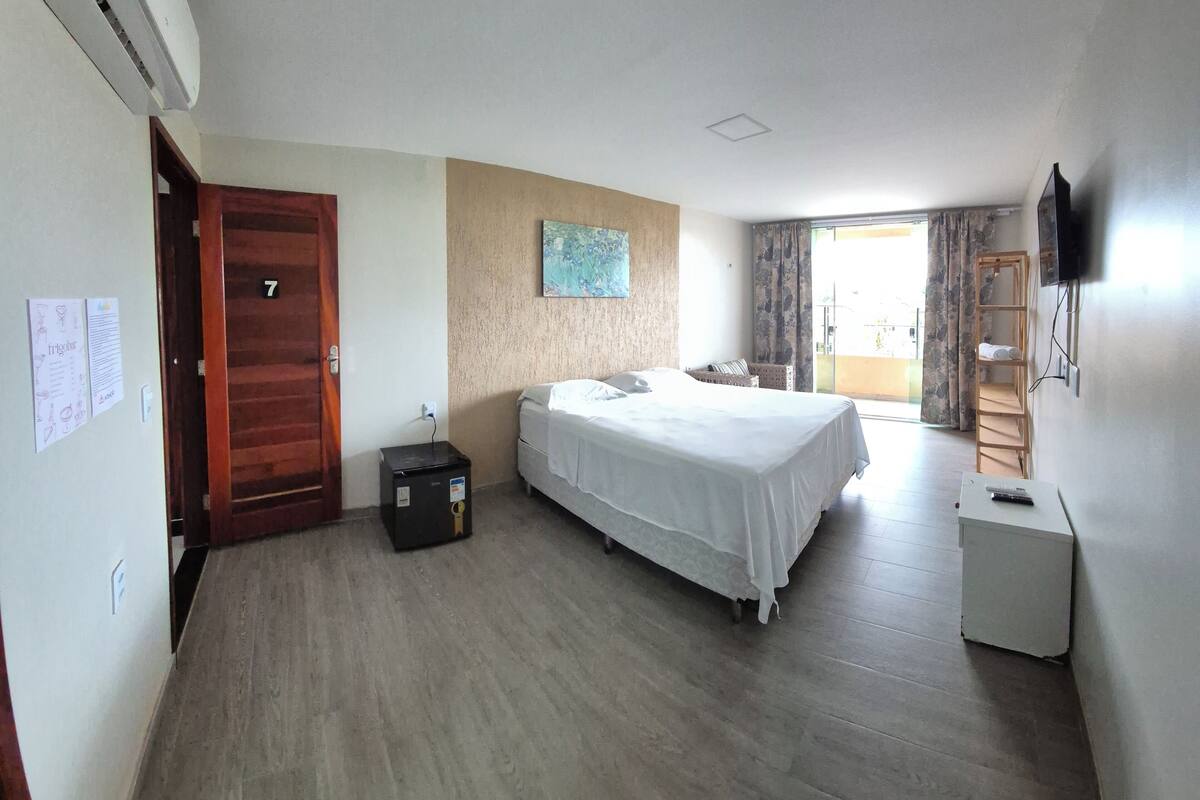 A hotel room with a bed, a desk, a TV, and a balcony with curtains.