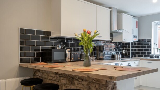 A modern kitchen with a central island, black and white tiled backsplash, and a vase of flowers. - Stylish house with Backyard + 4 min walk to Beach (Great Yarmouth)