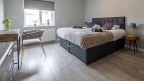 A modern bedroom with a bed, bedside table, lamp, and a window with blinds. - Stylish house with Backyard + 4 min walk to Beach (Great Yarmouth)