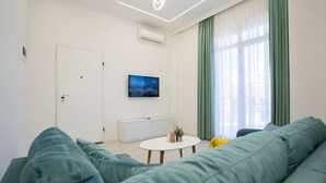 Ett modernt vardagsrum med en grön soffa, ett vitt soffbord och en platt-TV som är monterad på väggen.