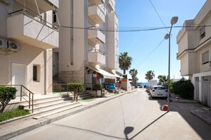 A multi-story building with balconies, a pizza shop on the ground floor, and parked cars along the street. - Athos Apartment by TOK (Durrës)