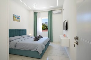 A bedroom with a bed, a bedside table, a TV, and a window with curtains. - Athos Apartment by TOK (Durrës)