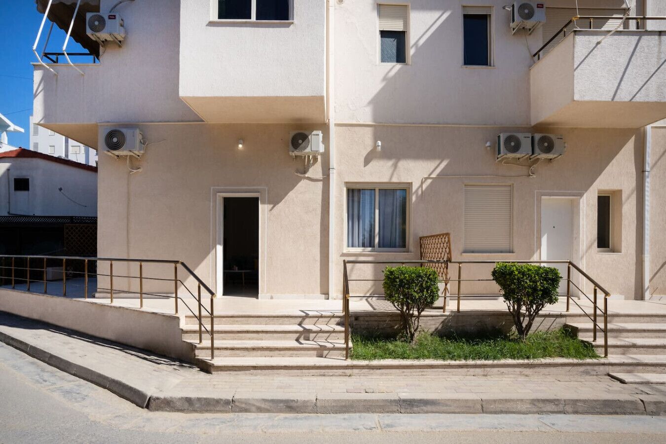 Un edificio de varios pisos con unidades de aire acondicionado, una escalera y un pequeño jardín con una silla y plantas.