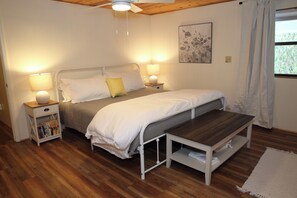 Un dormitorio con cama, mesitas de noche, un banco de madera y una ventana con cortinas.