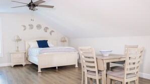 A bedroom with a bed, bedside tables, a ceiling fan, a dining table with chairs, and a rug.