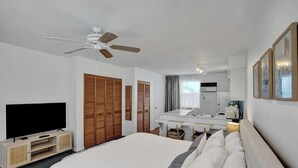Ein Hotelzimmer mit Bett, Fernseher, Deckenventilator, Schreibtisch mit Stuhl, Spiegel und Kleiderschrank.