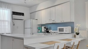 Eine moderne Küche mit weißen Schränken, einer eingebauten Mikrowelle und einem Essbereich mit weißem Tisch und Stühlen.