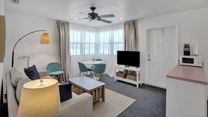 Ein modernes Wohnzimmer mit Deckenventilator, Flachbildfernseher, Essbereich mit Stühlen, Sofa und Lampe.