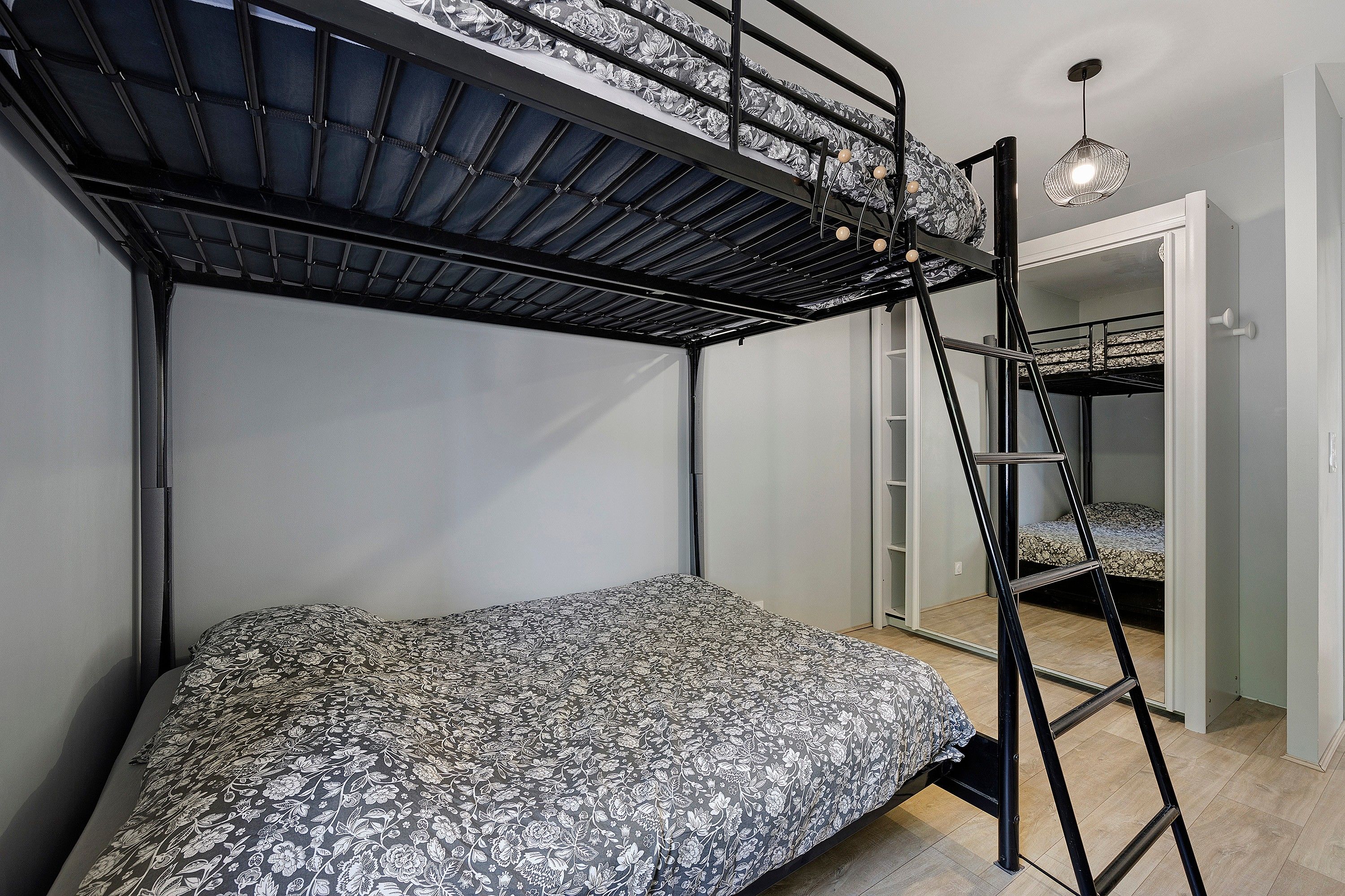Un lit superposé avec une échelle, un lit simple et un luminaire suspendu dans une pièce aux murs blancs.