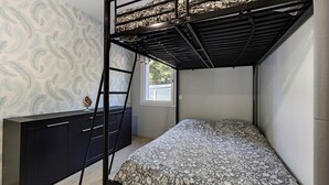 Uma cama de beliche com escada, uma cômoda e uma janela com vista para árvores.