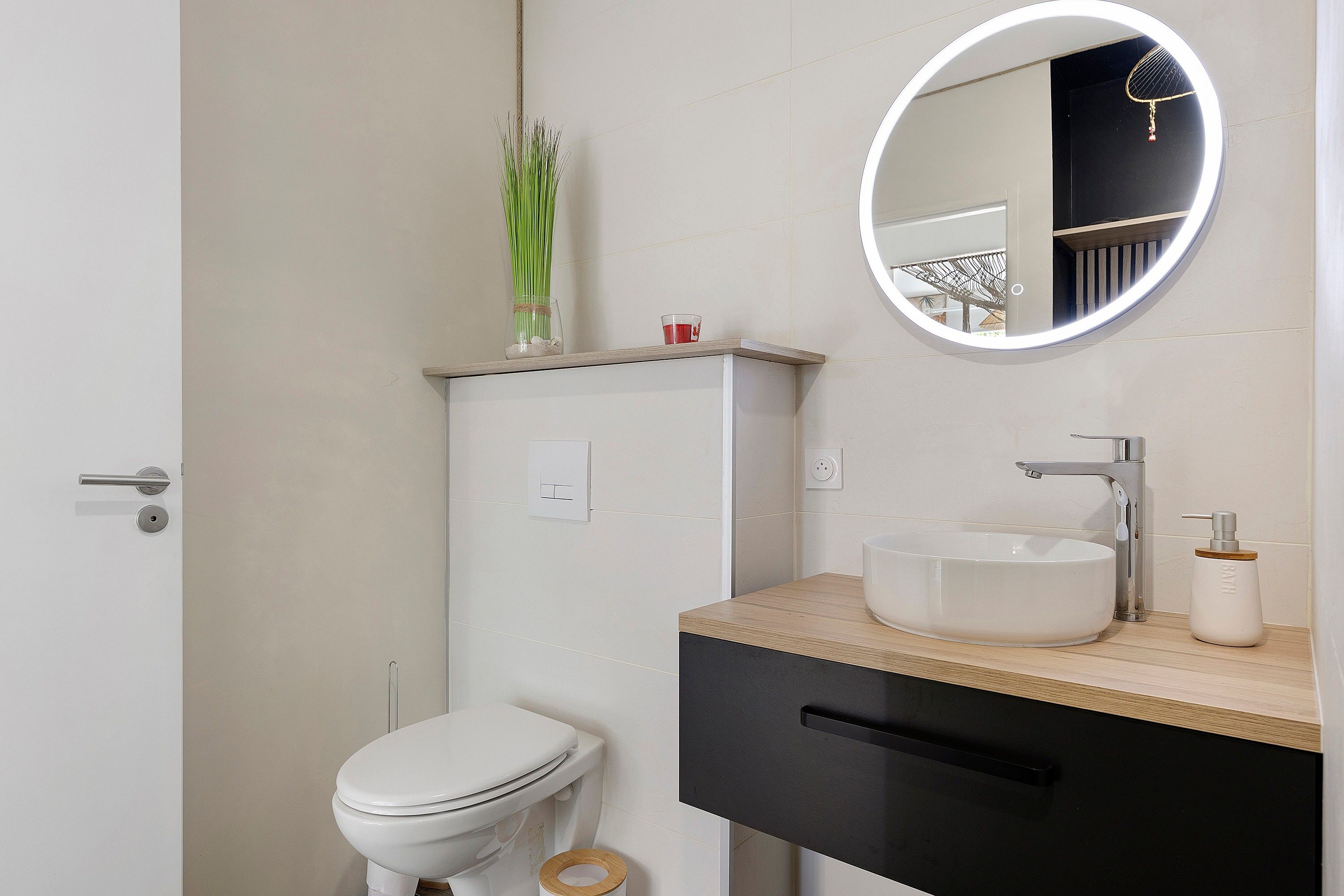 A bathroom with a toilet, a sink, a mirror, and a small plant on the vanity.