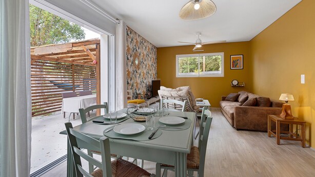 Uma sala de jantar com uma mesa posta para quatro pessoas, um sofá e um ventilador de teto.