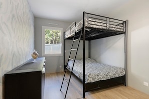 A bunk bed with a ladder, a small table with a glass container, and a window with a view of trees.
