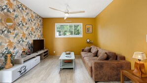 Uma sala de estar com televisão, sofá, mesa de centro e ventoinha no teto.
