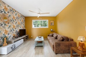 Ein Wohnzimmer mit Fernseher, Sofa, Couchtisch und Deckenventilator.