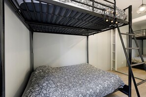 En våningssäng med ett mönstrat överkast, en stege och en hängande lampa.