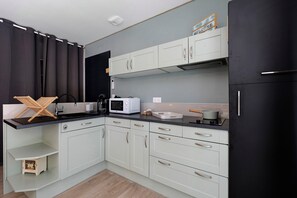 Eine kleine Küche mit weißen Schränken, einer Mikrowelle und einem schwarzen Kühlschrank.