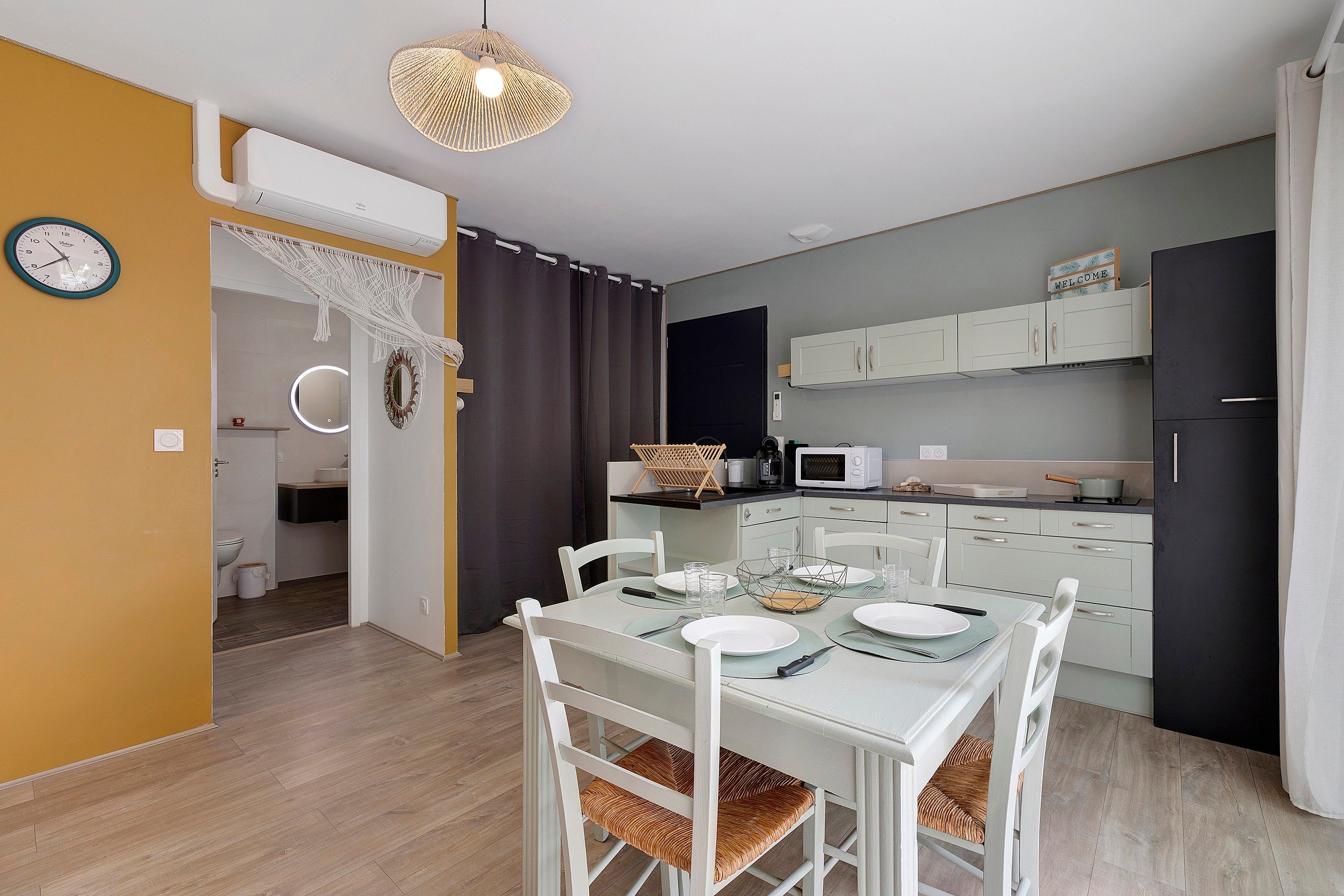 Een moderne keuken met witte kasten, een eettafel gedekt voor twee personen en een hanglamp.