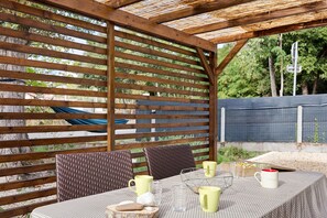 En uteplats med en träpergola, möbler av rotting och ett bord dukat med muggar och glas.
