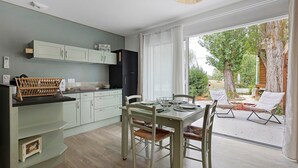 Cozinha moderna com armários verde claro, área de refeições com mesa e cadeiras, e vista para o exterior através de grandes janelas.