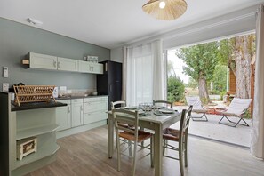 Eine moderne Küche mit hellgrünen Schränken, ein Essbereich mit Tisch und Stühlen sowie ein Blick ins Freie durch große Fenster.