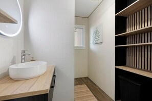 Ett modernt badrum med en stor, vit tvättställ, en spegel med inbyggd belysning och ett badrumsskåp i trä.