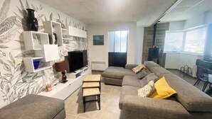 A living room with a sofa, TV, shelves, and a window. - Charming house in the heart of L'Aiguillon-sur-mer - 8 people (L'Aiguillon-la-Presqu'île)