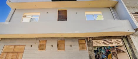 A hotel building with a sign indicating it is company-serviced. There are multiple windows on the facade, and a small outdoor area with a colorful mural.