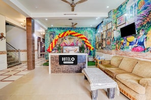 A hotel lobby with a reception desk, a sofa, a bench, a staircase, and a mural on the wall. - Hotel O Prem Mandir (Mathura)