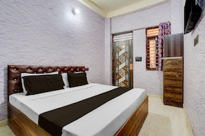 A bedroom with a bed, a wooden headboard, a wall-mounted TV, and a door with patterned glass. - Hotel O Prem Mandir (Mathura)