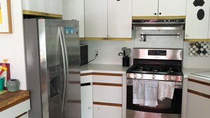 Una cocina con armarios blancos, un refrigerador de acero inoxidable, una estufa y piso de baldosas.