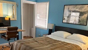Un dormitorio con cama, escritorio y silla, ventana con persianas y un cuadro en la pared.