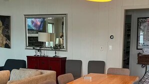 Un comedor con una mesa de madera, sillas tapizadas grises y una lámpara colgante naranja.
