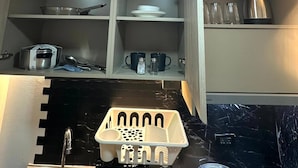 A kitchen with a sink, a dish rack, and cabinets containing dishes and utensils. - Smart Studio Appartment Near Old Town Phuket (Phuket)