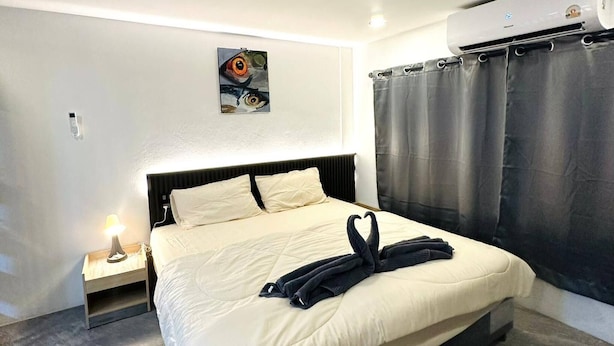A modern hotel room with a large bed, a headboard, a nightstand, a lamp, a painting on the wall, and an air conditioning unit. - Smart Studio Appartment Near Old Town Phuket (Phuket)