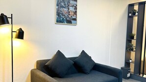 A modern living room with a dark sofa, a glass coffee table, a floor lamp, and a framed picture on the wall. - Smart Studio Appartment Near Old Town Phuket (Phuket)