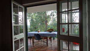 An open door leading to a patio with a table and chairs, a bowl of fruit, and a view of trees.