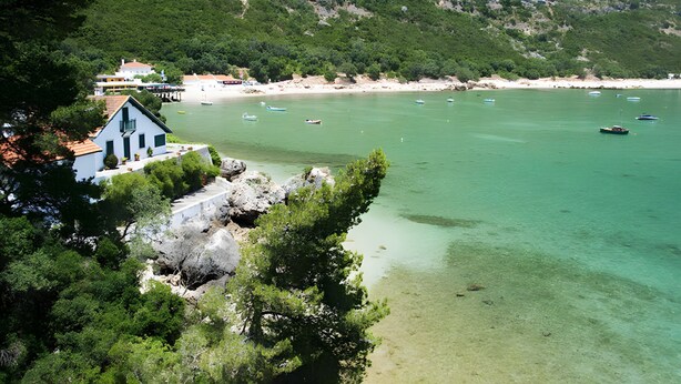 A coastal area with clear turquoise waters, boats, and a building with a red roof.