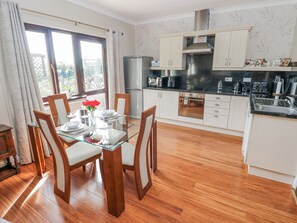 A modern kitchen with white cabinets, a stainless steel range hood, and a dining area with a glass table and wooden chairs. - Harvest Hill (Haverfordwest)