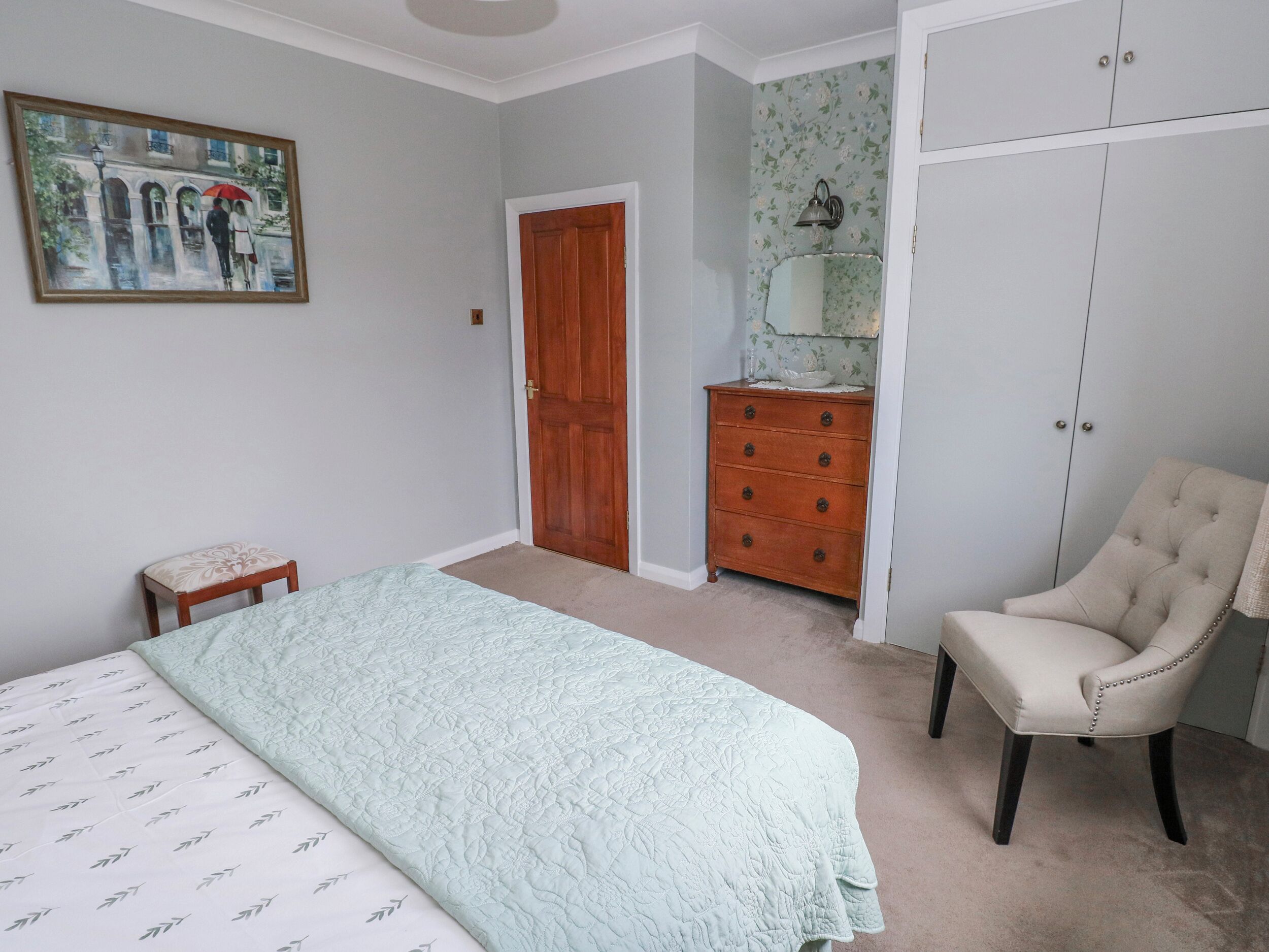 A bedroom with a bed, a chair, a dresser, a door, and a painting on the wall.