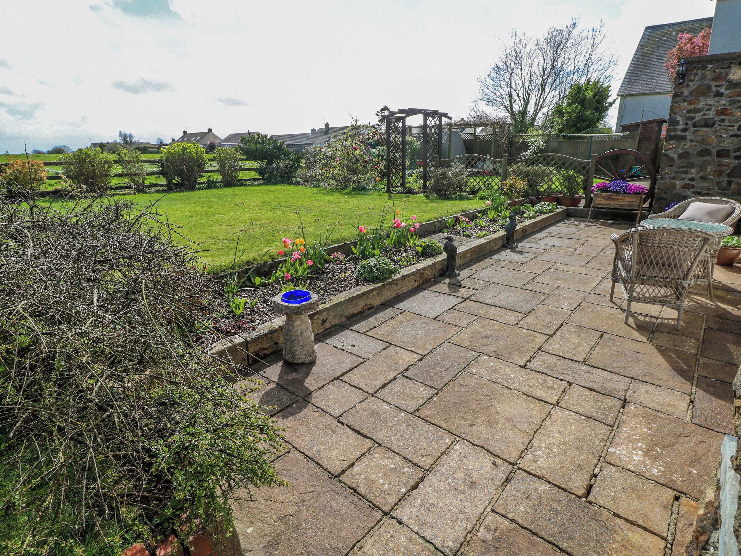Une terrasse carrelée, un jardin fleuri et une pergola en bois.