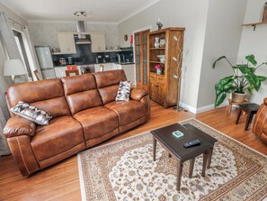 A living room with a brown leather sofa, a coffee table, a patterned rug, a wooden cabinet, and a potted plant. - Harvest Hill (Haverfordwest)