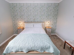 Une chambre à coucher avec un lit, deux tables de chevet avec des lampes, un papier peint à motifs floraux et une tête de lit en bois.