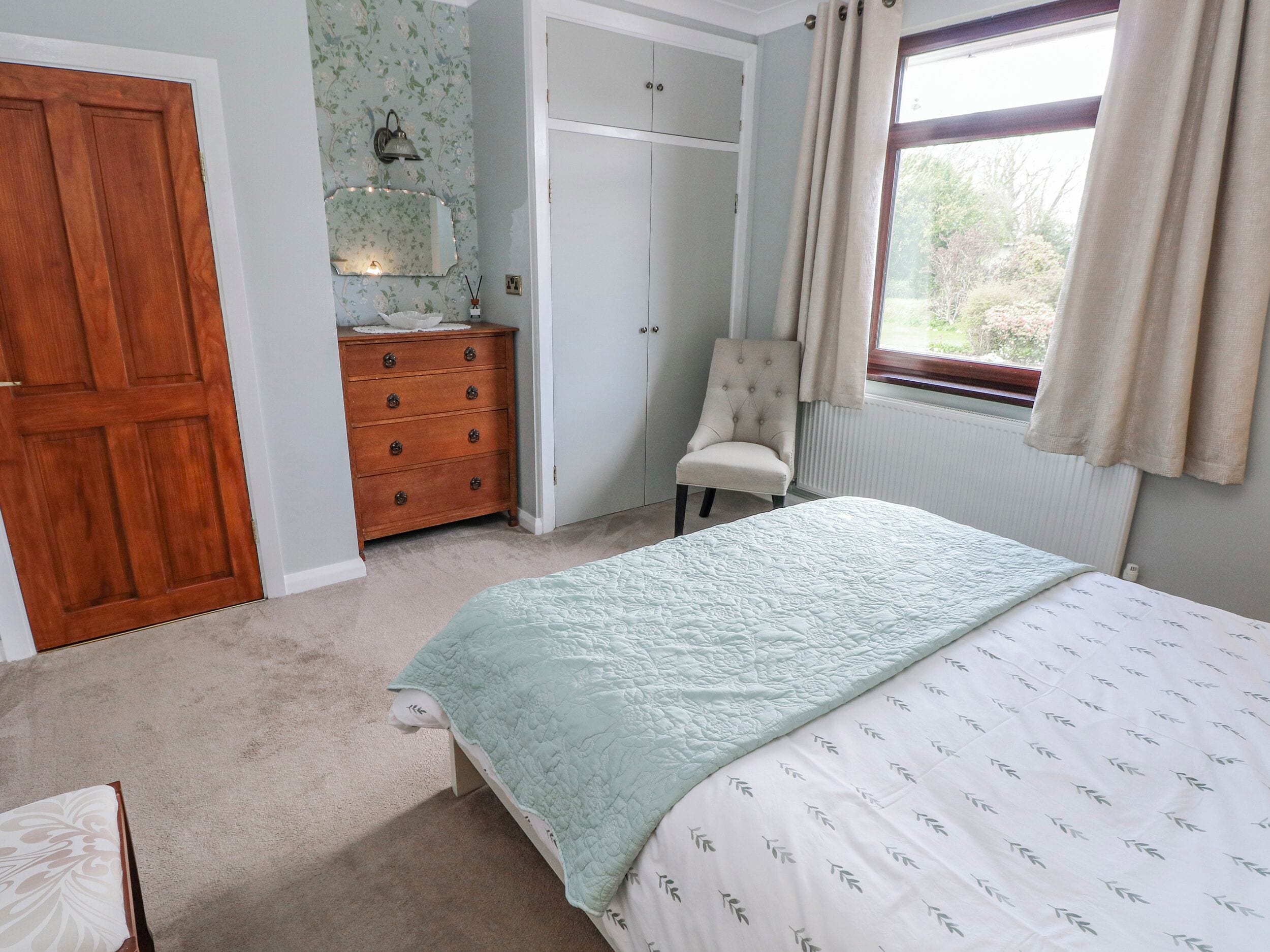 A bedroom with a bed, a dresser, a chair, a wardrobe, and a window with curtains.
