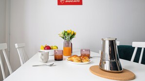 En frukostuppsättning med en kaffekanna, croissanter, frukt och juice på ett vitt bord.