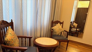 Ein Zimmer mit zwei Holzstühlen mit gepolsterten Sitzen, einem runden Holztisch und einem großen Spiegel an der Wand.