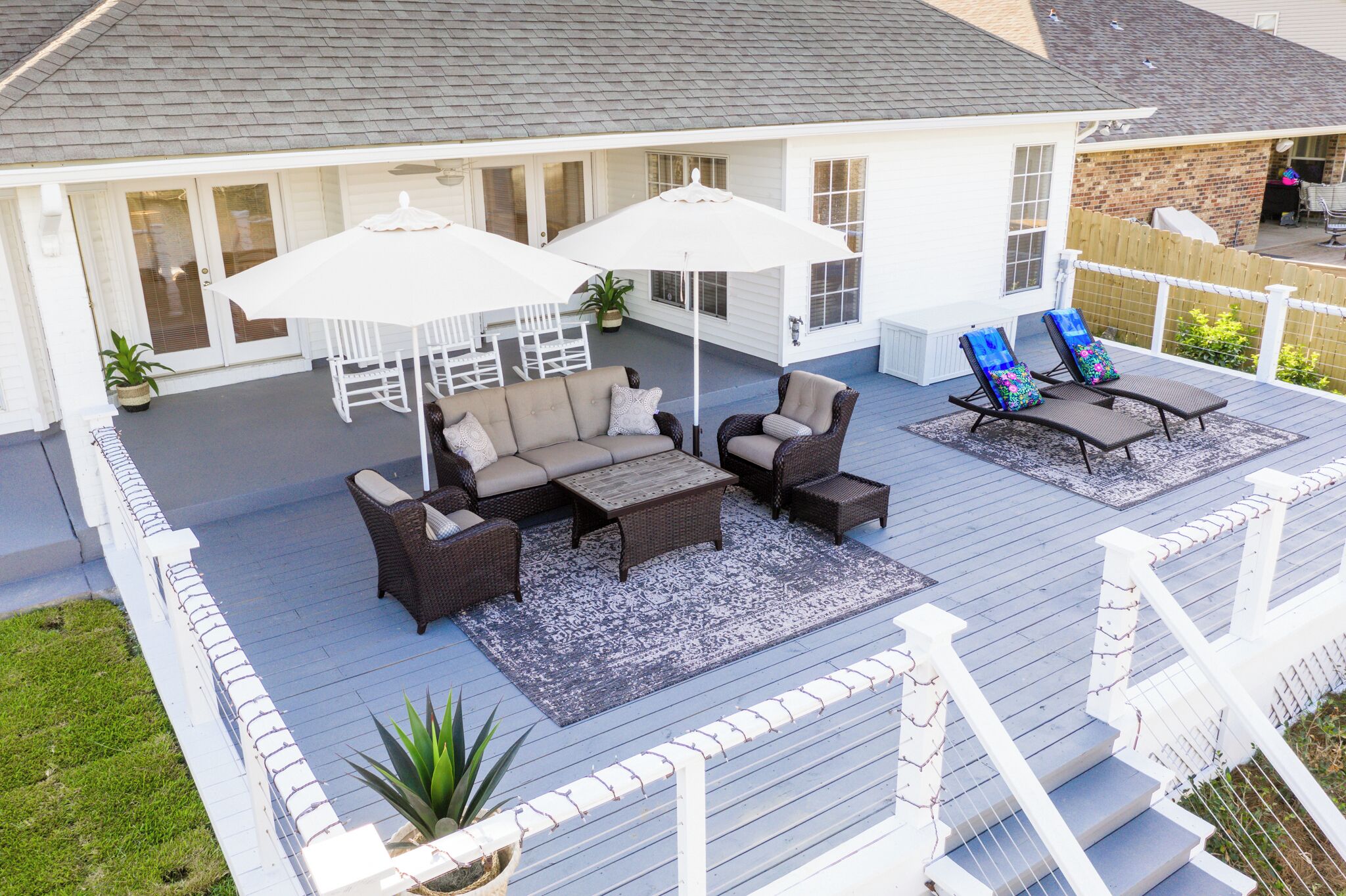 Eine überdachte Terrasse mit Gartenmöbeln, darunter eine Couch, Stühle und ein Tisch, umgeben von weißen Sonnenschirmen.